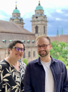 Stephanie Harkort und Benjamin Müller lächeln in die Kamera. Im Hintergrund ist die Nürnberger Egidienkirche mit ihren Türmen zu sehen.